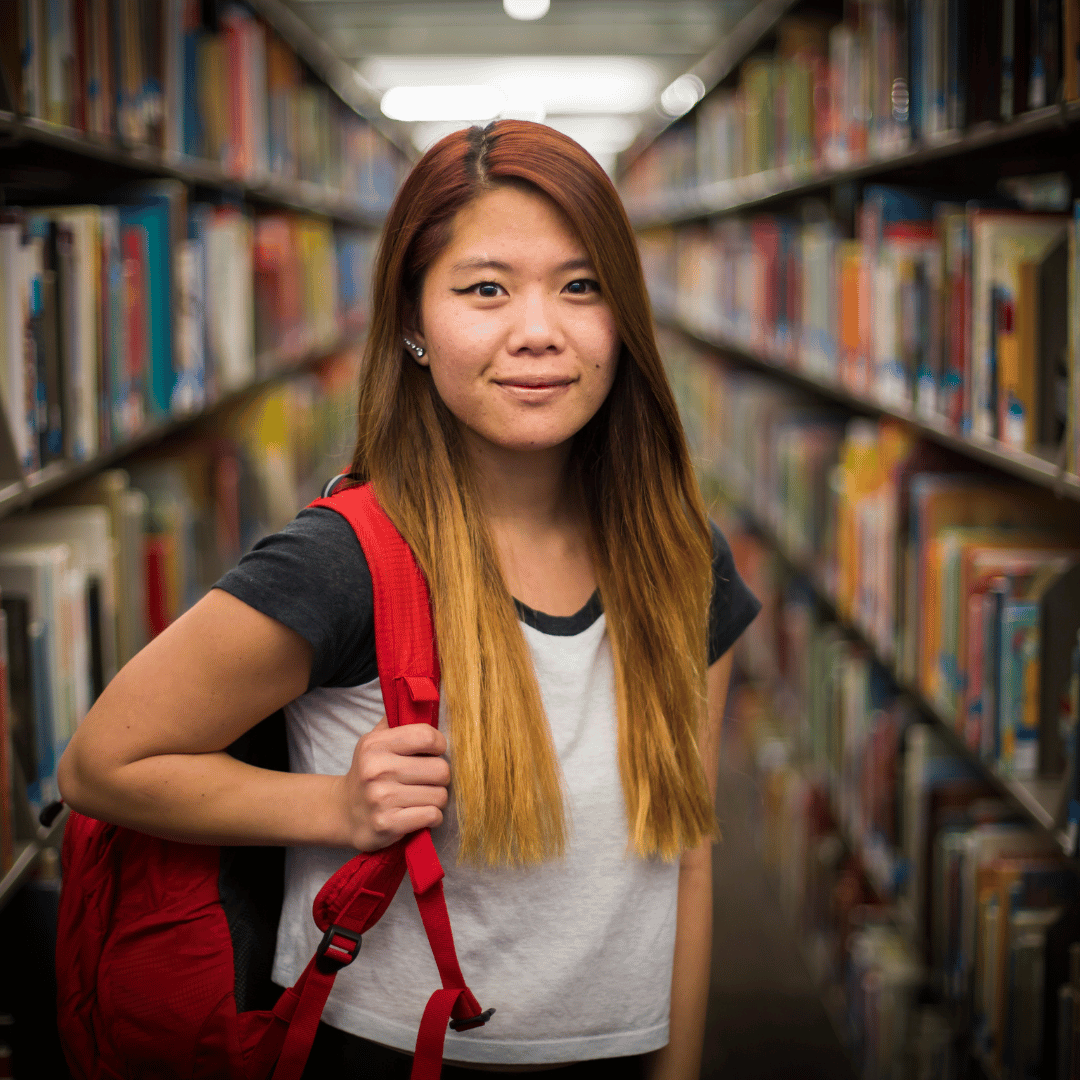 student smiling with their back pack in the library
